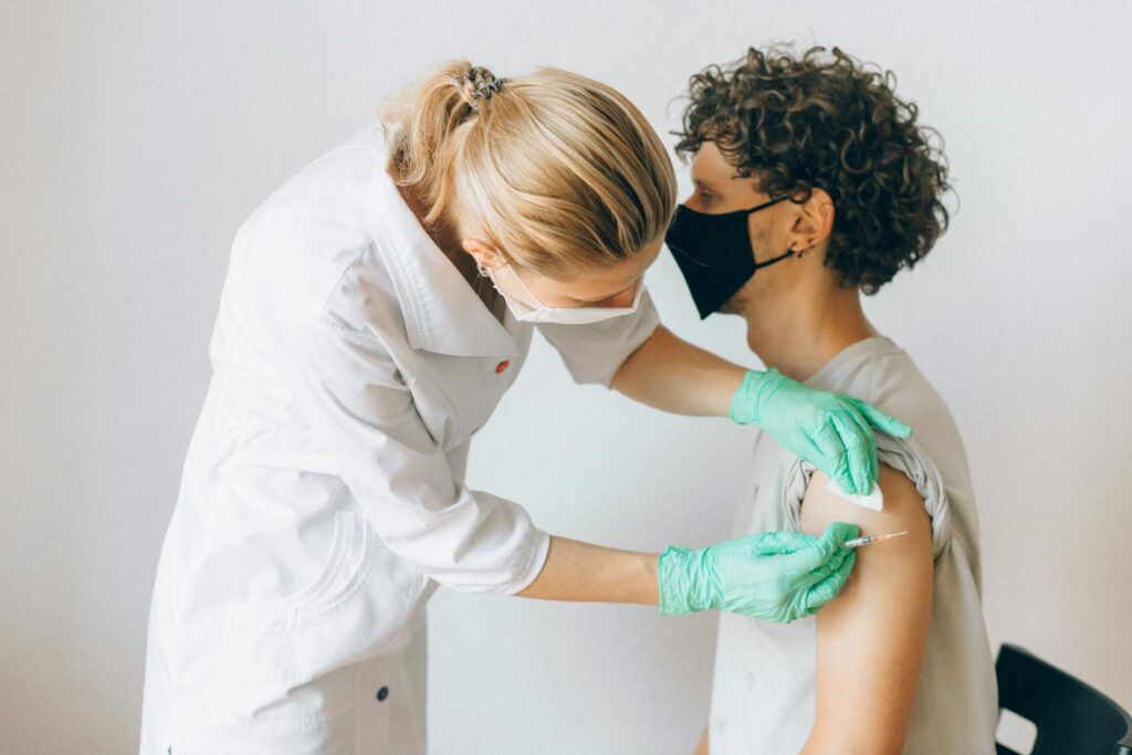 A healthcare worker gives a vaccine shot to a patient wearing a mask, highlighting medical safety and health precautions.