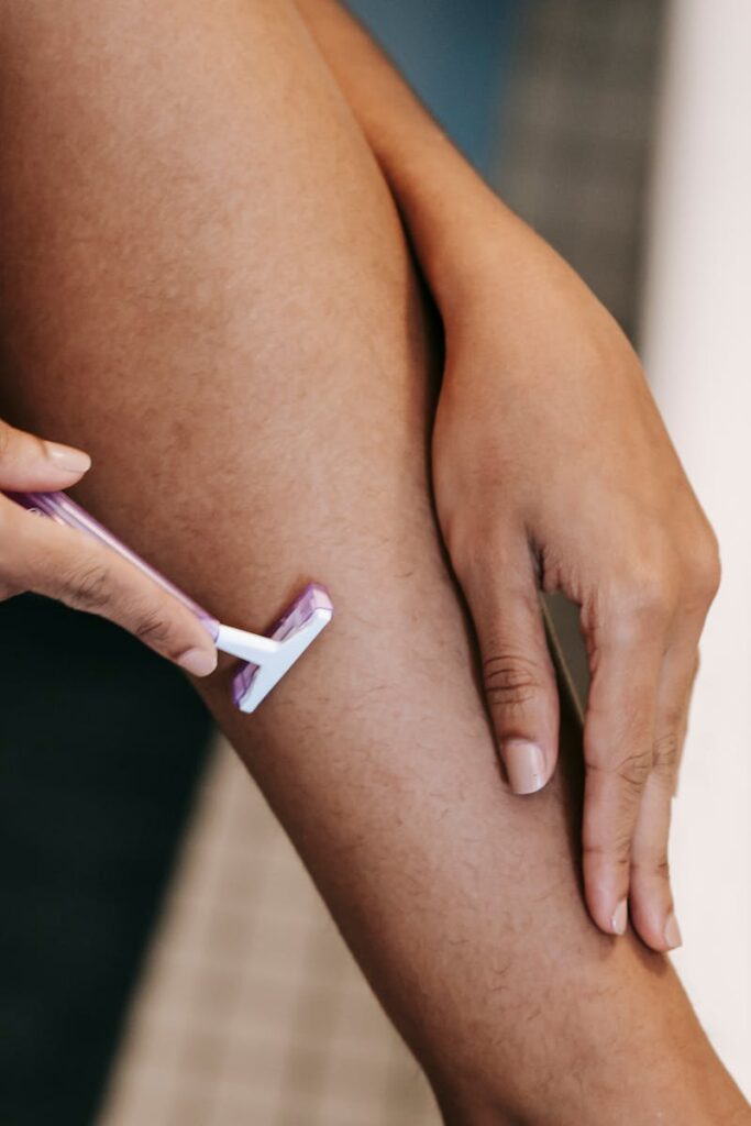 Crop ethnic woman shaving leg with disposable razor